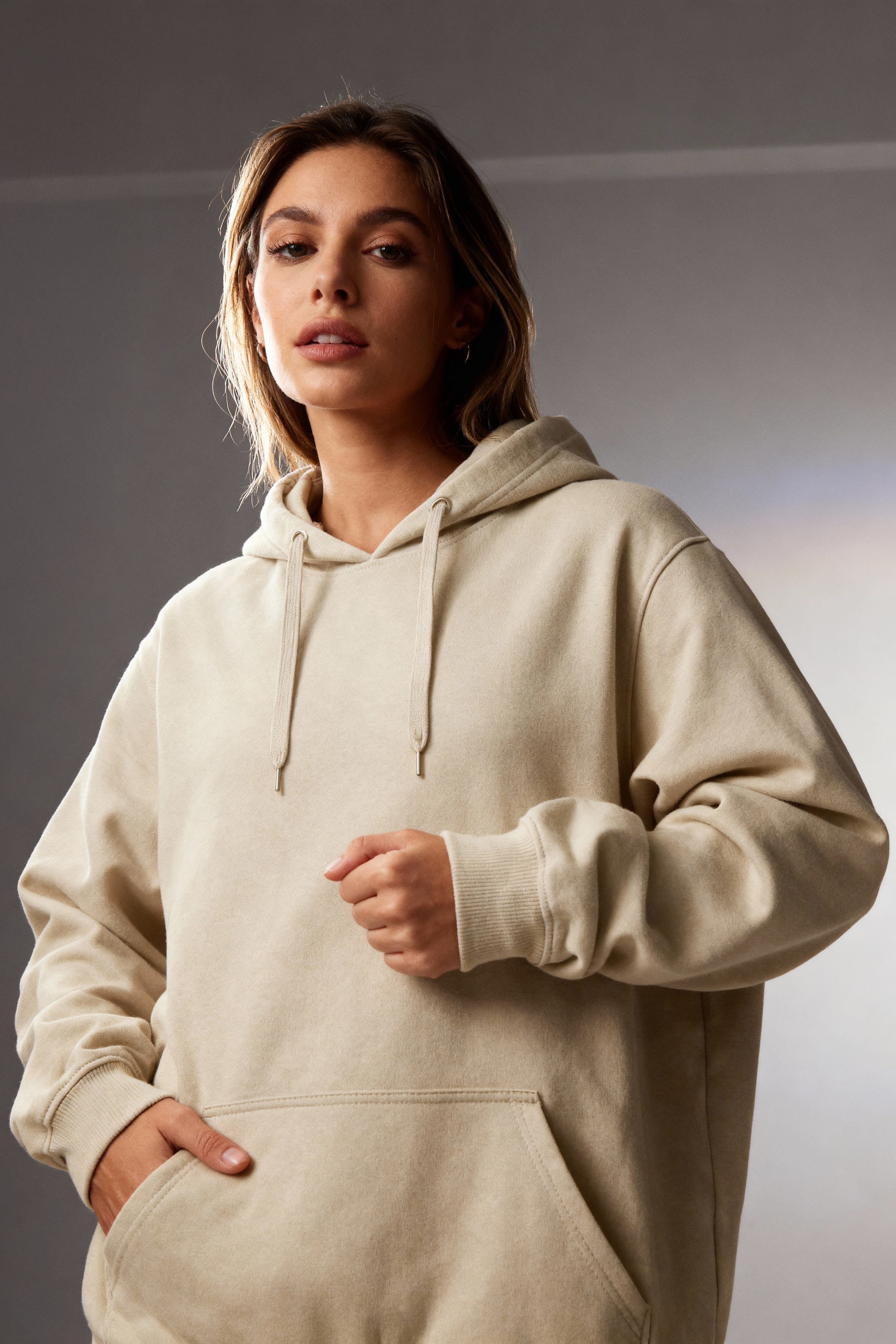Woman wearing a beige hoodie against a neutral background